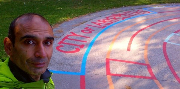 HiMY SYeD, smiling beside "City of Labyrinths" painted within the outer most lanes of a Labyrinth he painted in the wading pool/splash pad opposite in Earl Grey Senior Public School, which he attended for Grades 7 and 8, located in East End Toronto.