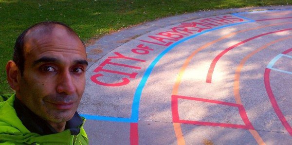 HiMY SYeD, smiling beside "City of Labyrinths" painted within the outer most lanes of a Labyrinth he painted in the wading pool/splash pad opposite in Earl Grey Senior Public School, which he attended for Grades 7 and 8, located in East End Toronto.