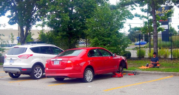 Red Car jacked up with front-right tire removed in parking lot in a gas station in Mississauga, Ontario on Friday afternoon September 4 2026.
