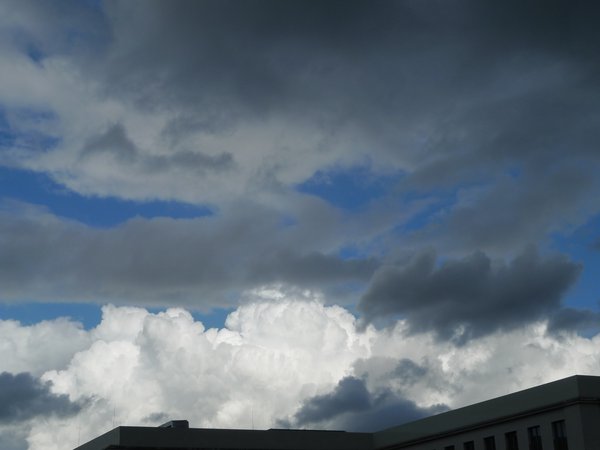Ausblick aus dem dritten Stock über das gerade noch so angeschnittene Dach der "Annenhöfe", in den Himmel, an dem sich hell und dunkle Wolken, sowie dazwischen ein Streifen des blauen Himmels zeigt.