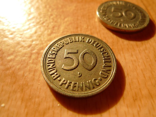 Auf dem Boden liegen zwei 50 Pfennig-Münzen, eine im Makro-Fokus im Vordergrund, eine rechts im oberen Eck, unscharf im Hintergrund.