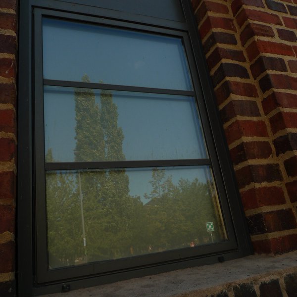 Das Gebäude ist außen mit alten roten Klinkersteinen verkleidet. Während der Sanierung wurden die originalen Fenster gegen exakte Nachbauten ausgetauscht und haben wieder einen dunklen Rahmen im industriellen Design. In den Sprossenfenstern spiegelt sich ein großer, schmaler Baum vor dem dahinter liegenden blauen Himmel.
