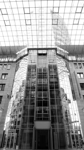 Vertikale Panorama-Aufnahme in schwarz-weiß des gesamten Turmes, wobei der Turm über der Atrium-Verglasung (im 7. Stockwerk) durch die Morgensonne überstrahlt wird und damit kaum zu erkennen ist.