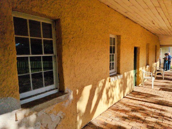 Close-up of the front of the house under the verandah. The cream-coloured render on the brick walls is chipping away.