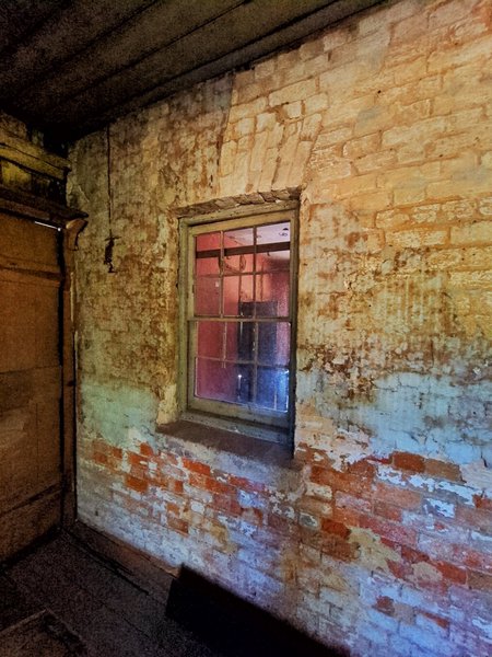 A small room with a wooden ceiling. The window looks into the pink kitchen from earlier.