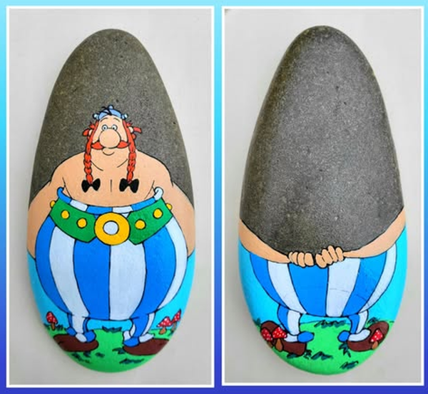 Das Bild zeigt einen kleinen, länglichen und nach oben abgerundeten Stein, dessen Form an einen Hinkelstein erinnert. Der Stein wurde rundherum so bemalt, dass er selbst zum Körper von Obelix wird.
Auf der Vorderseite sind Obelix’ Gesicht mit den roten Zöpfen, sein nackter Oberkörper sowie der grüne Gürtel mit großer gelber Schnalle zu sehen. Darunter setzt sich seine typische blau-weiß gestreifte Hose bis zum unteren Rand des Steins fort. Seine Füße stehen auf einer kleinen grünen Wiese, die mit roten Pilzen und Blumen verziert ist. Der obere, dunkelgraue Teil des Steins bleibt weitgehend unbemalt und wirkt dadurch wie ein Hinkelstein, der hinter Obelix aufragt.
Die Rückseite löst den kleinen optischen Scherz auf: Dort fehlen Kopf und Oberkörper völlig. Stattdessen sieht man nur Obelix’ Arme, die sich von beiden Seiten um den grauen Stein legen. Seine Hände greifen hinter dem „Hinkelstein“ ineinander. Darunter sind wiederum die gestreifte Hose und seine Füße auf der Wiese zu erkennen.