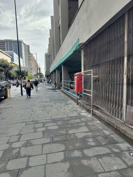 Rote, besprayter italienischer Briefkasten vor einer Gitterstruktur in einer mit Betonplatten gepflästerten Seitenstrasse.