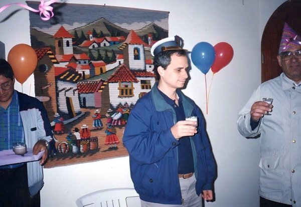 Imagen de una fiesta pochísima. Decoración desangelada. En el centro, el joven Prevost sostiene una bebida en un vasito pequeño mientras sonríe mecánicamente con la vista perdida. Lleva una gorra pequeña a modo de gorro de fiesta. Se ven otras dos personas, uno sostiene una copita y otro porta una bandeja. Todo es muy triste, como La Vida.