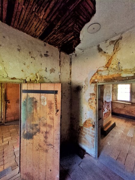 A small room where most of the ceiling has collapsed. The door to the previous room is on the right. Another room is on the left.